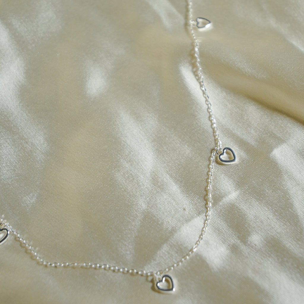 Silver heart-shaped necklace on a beige fabric background