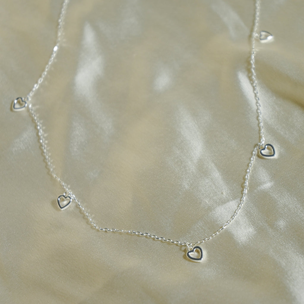 Silver necklace with heart-shaped charms on a beige fabric background