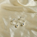 Silver hoop earrings with small spherical charms on a beige fabric background