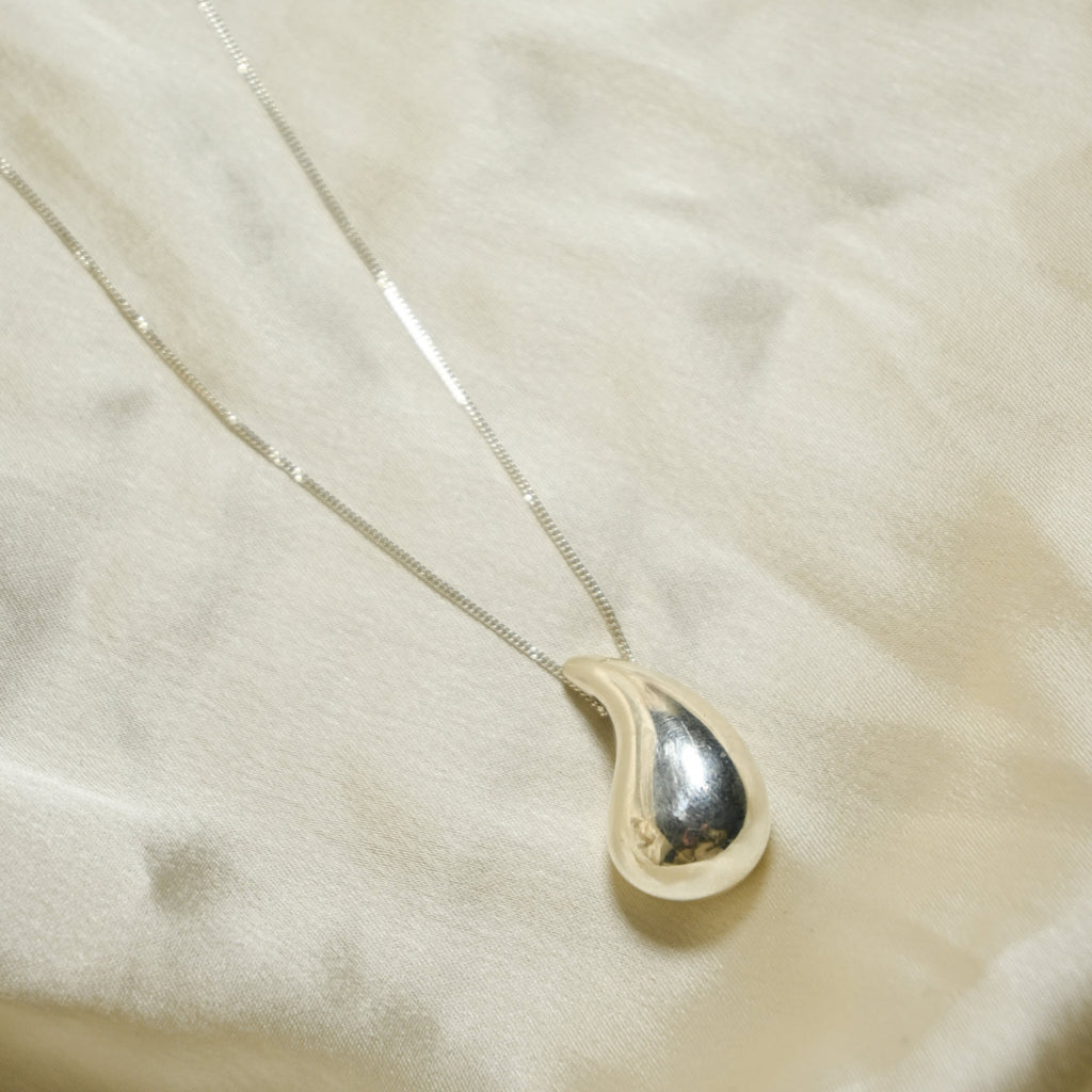 Teardrop-shaped pendant on a chain against a beige fabric background