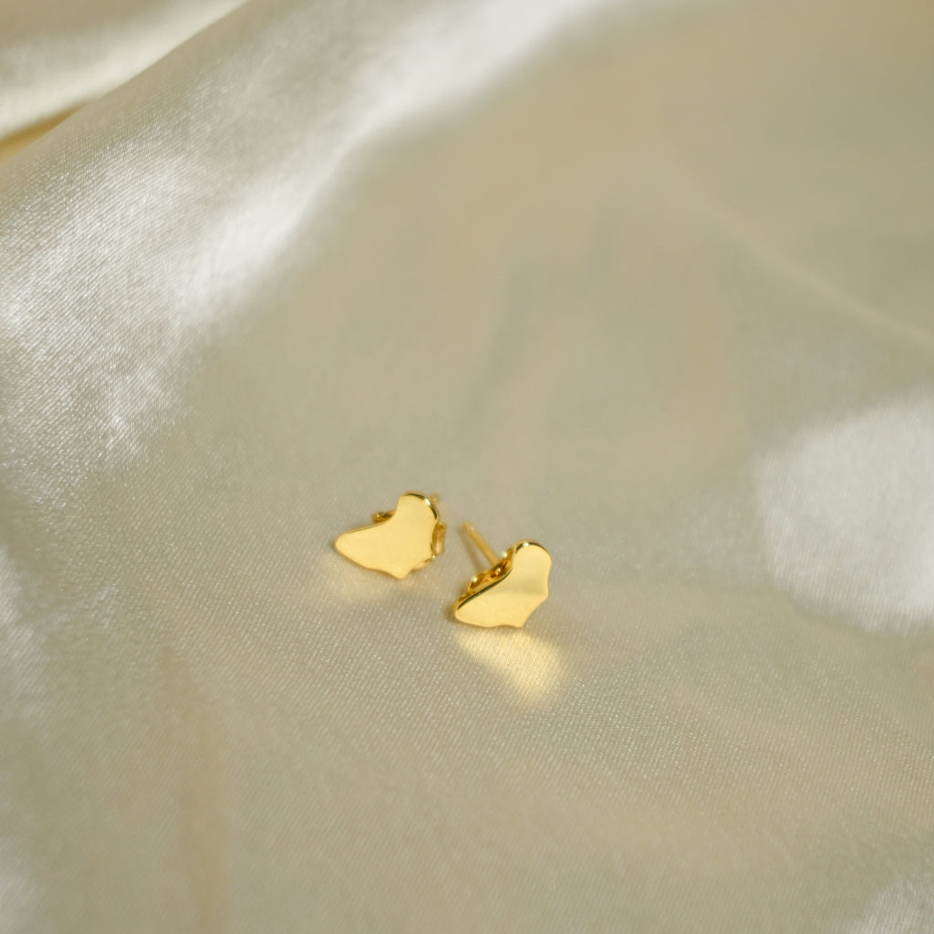 Gold heart-shaped earrings on a beige fabric background