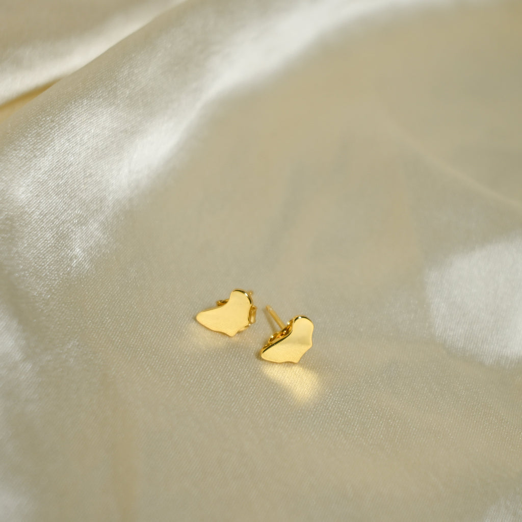 Gold heart-shaped earrings on a soft beige fabric background