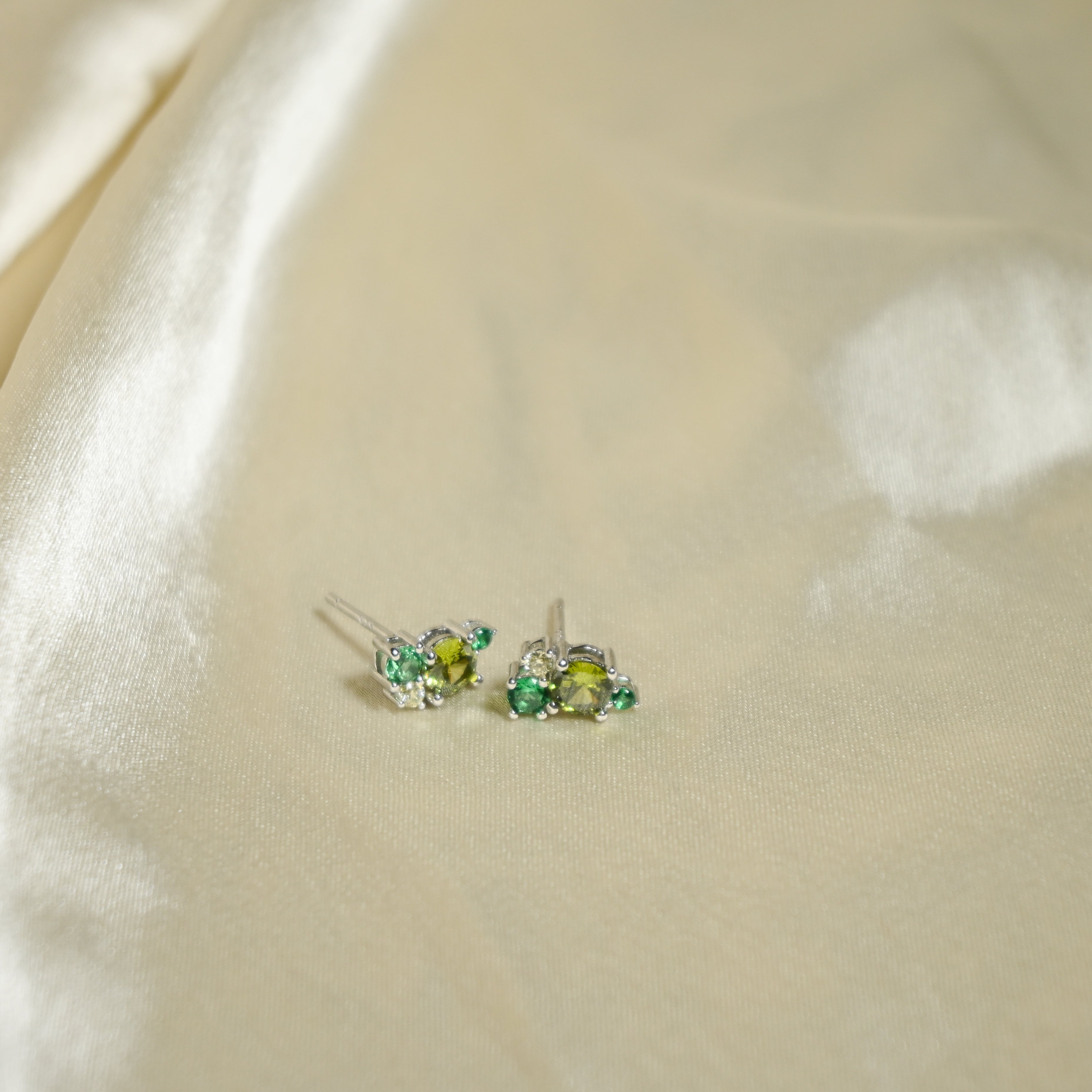 Pair of earrings with green gemstones on a beige fabric background