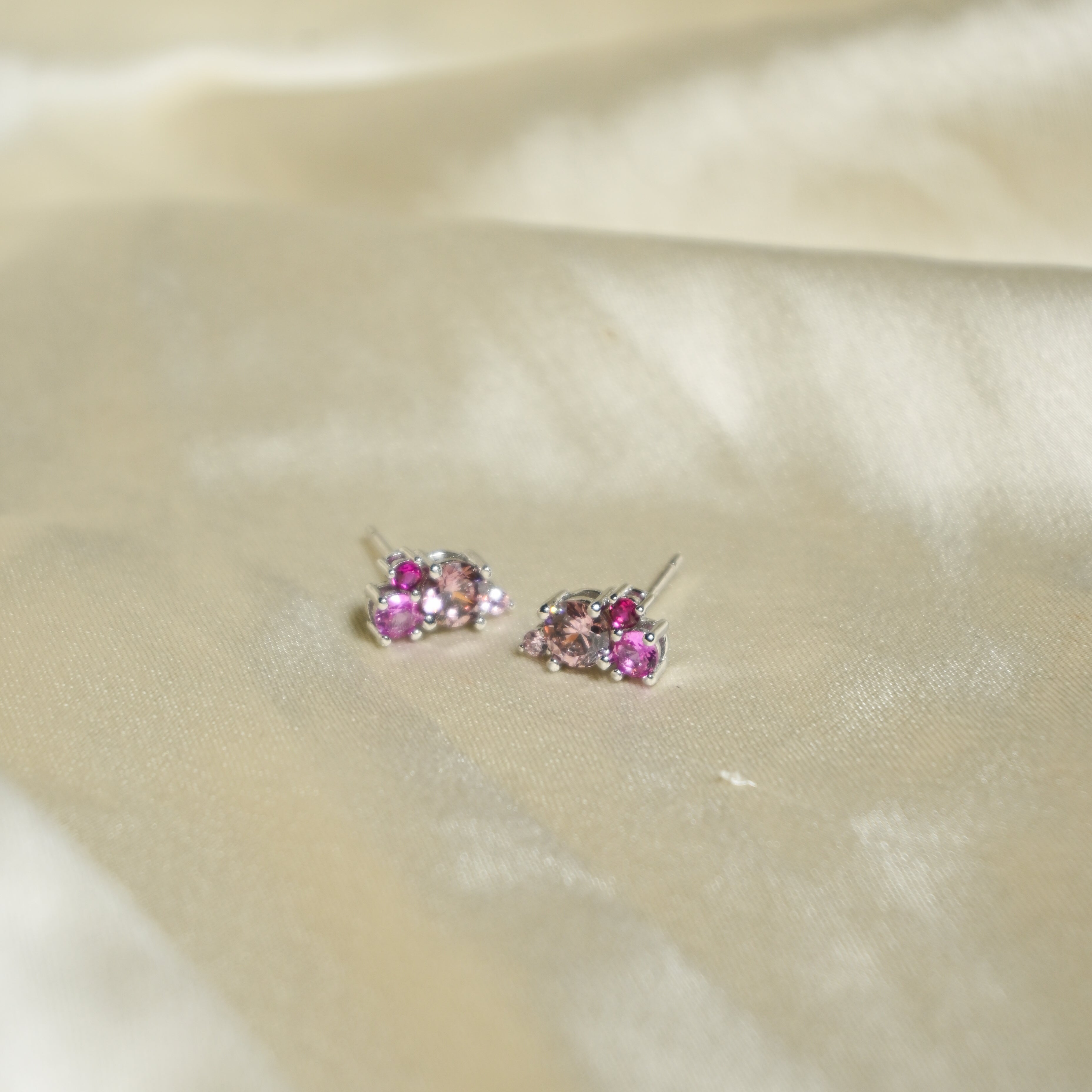 Pair of earrings with pink gemstones on a beige fabric background
