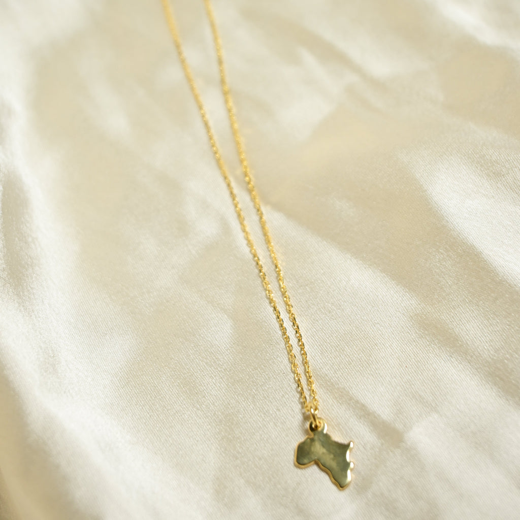 Gold necklace with a green stone pendant on a soft beige fabric background