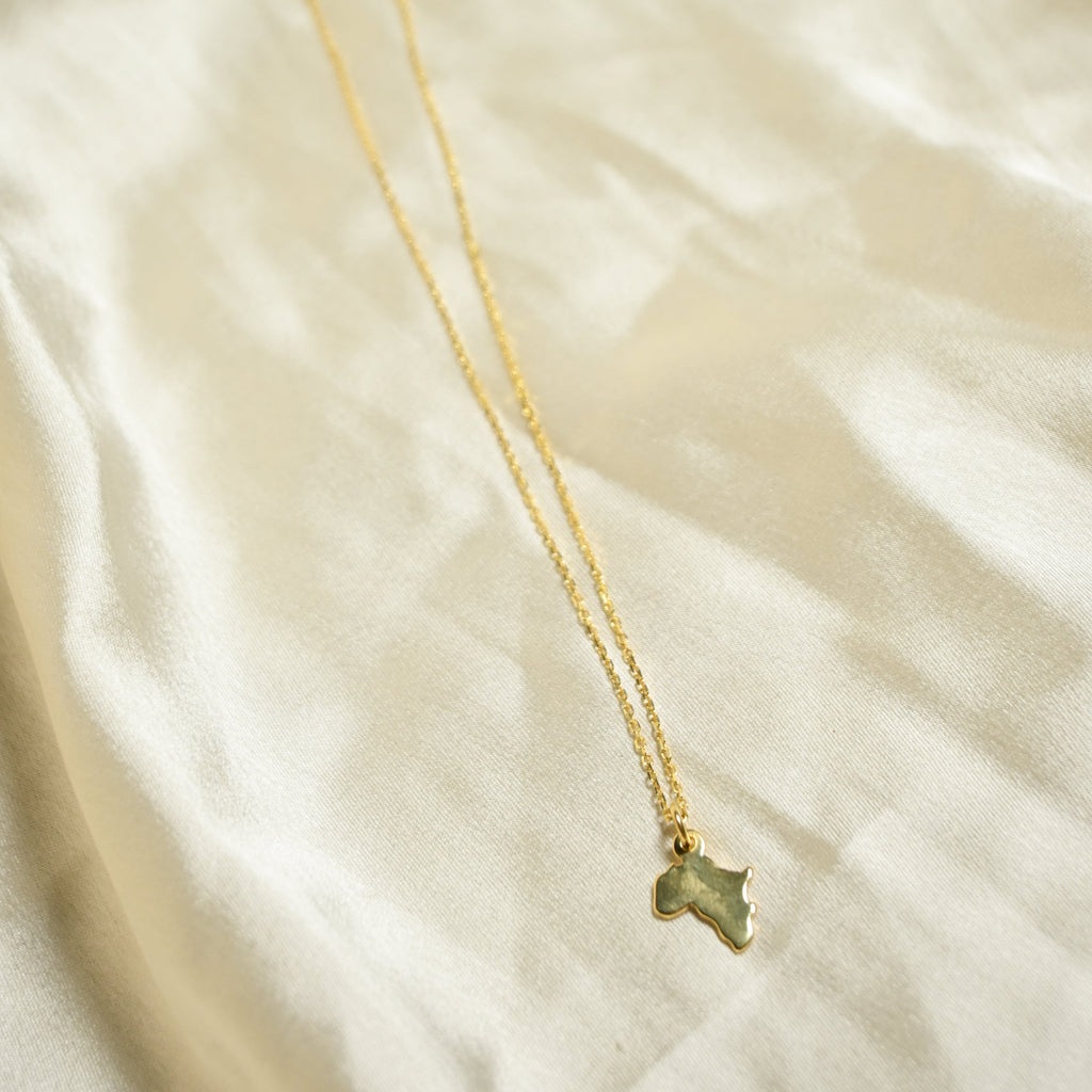 Gold necklace with a green pendant on a beige fabric background
