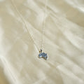 Small blue pendant on a chain against a beige fabric background