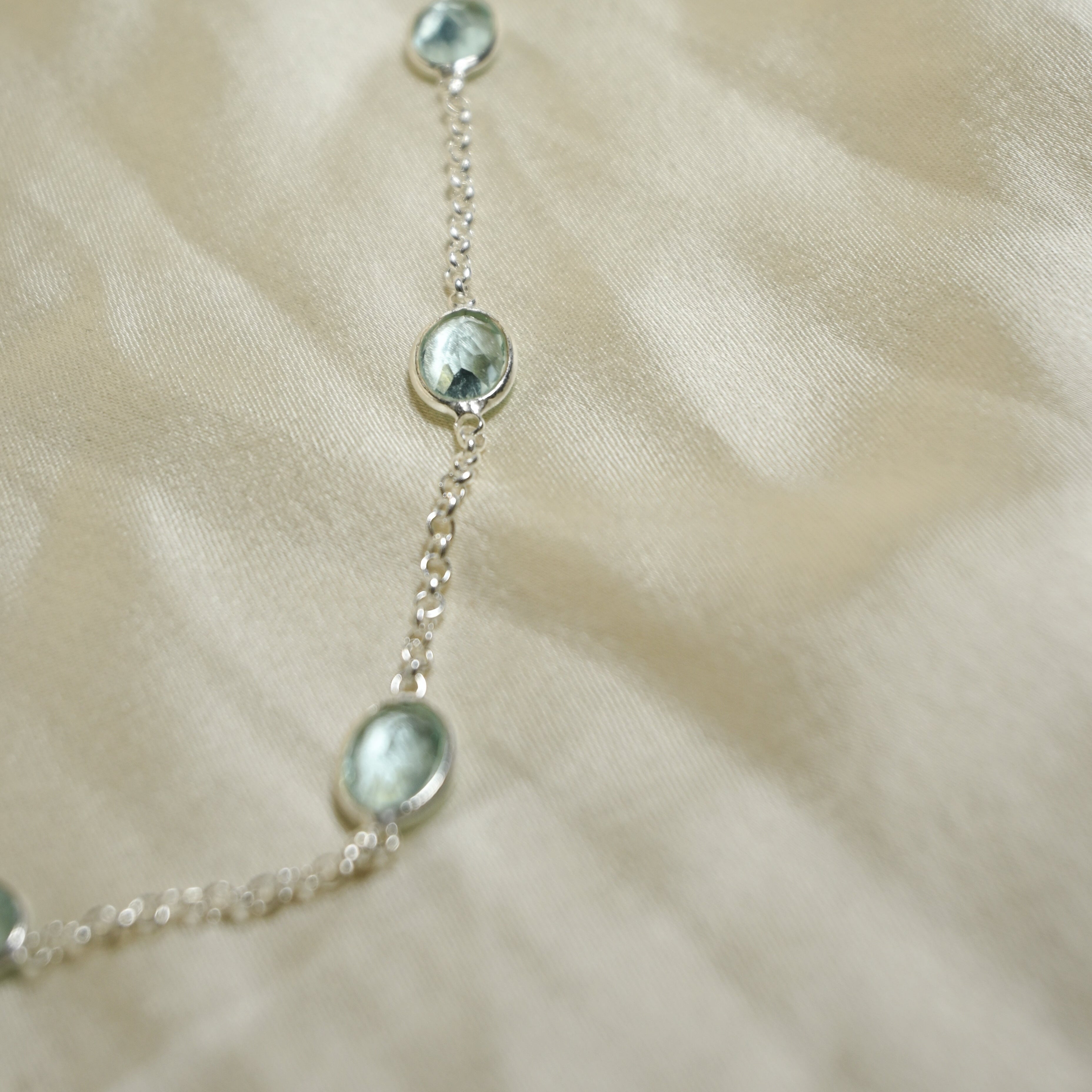 Silver chain necklace with small round pendants on a beige fabric background