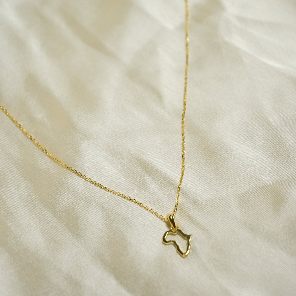 Gold necklace with a small pendant on a soft beige fabric background