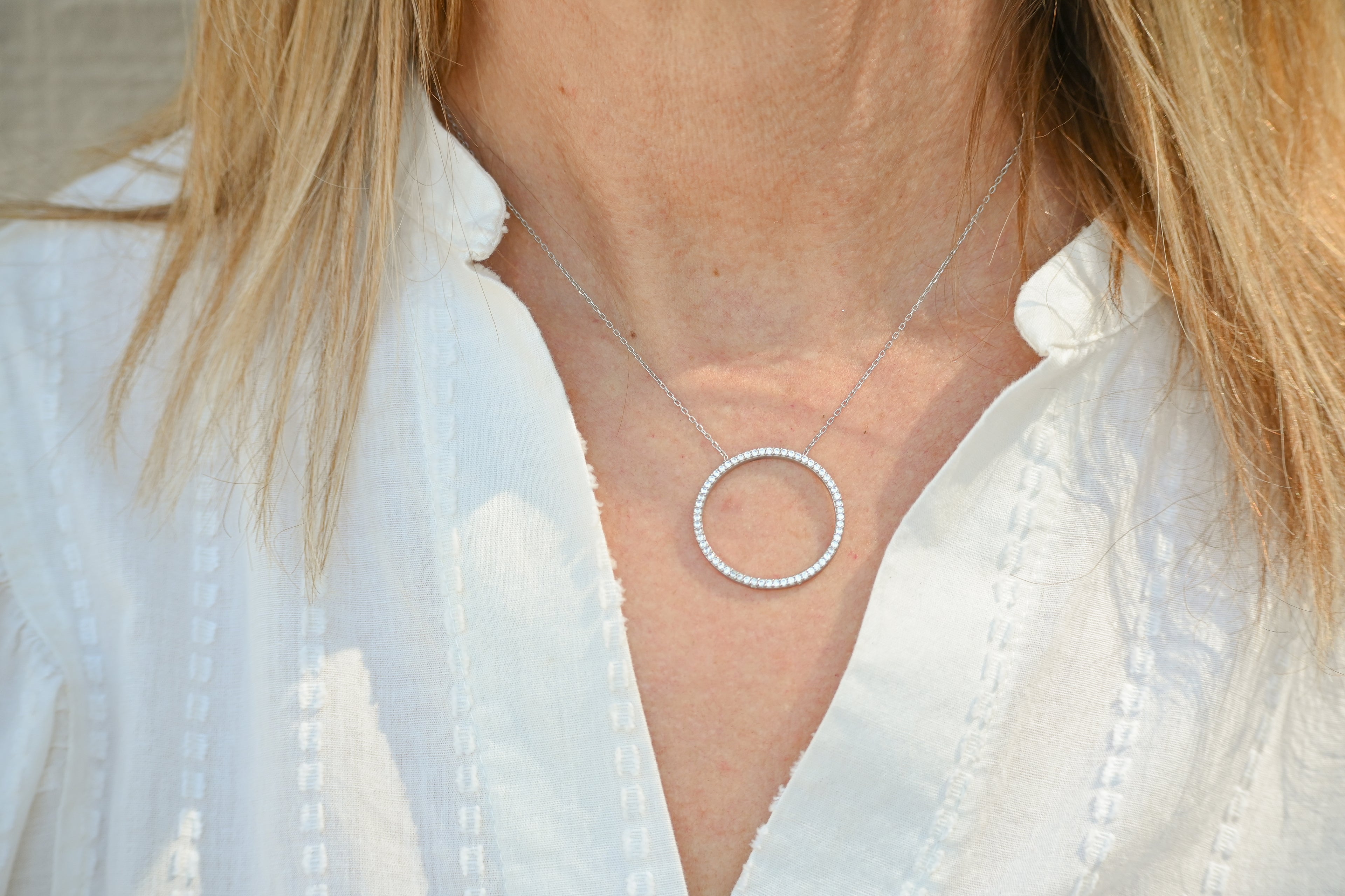 Close-up of a silver necklace with a circular pendant worn by a person in a white shirt.