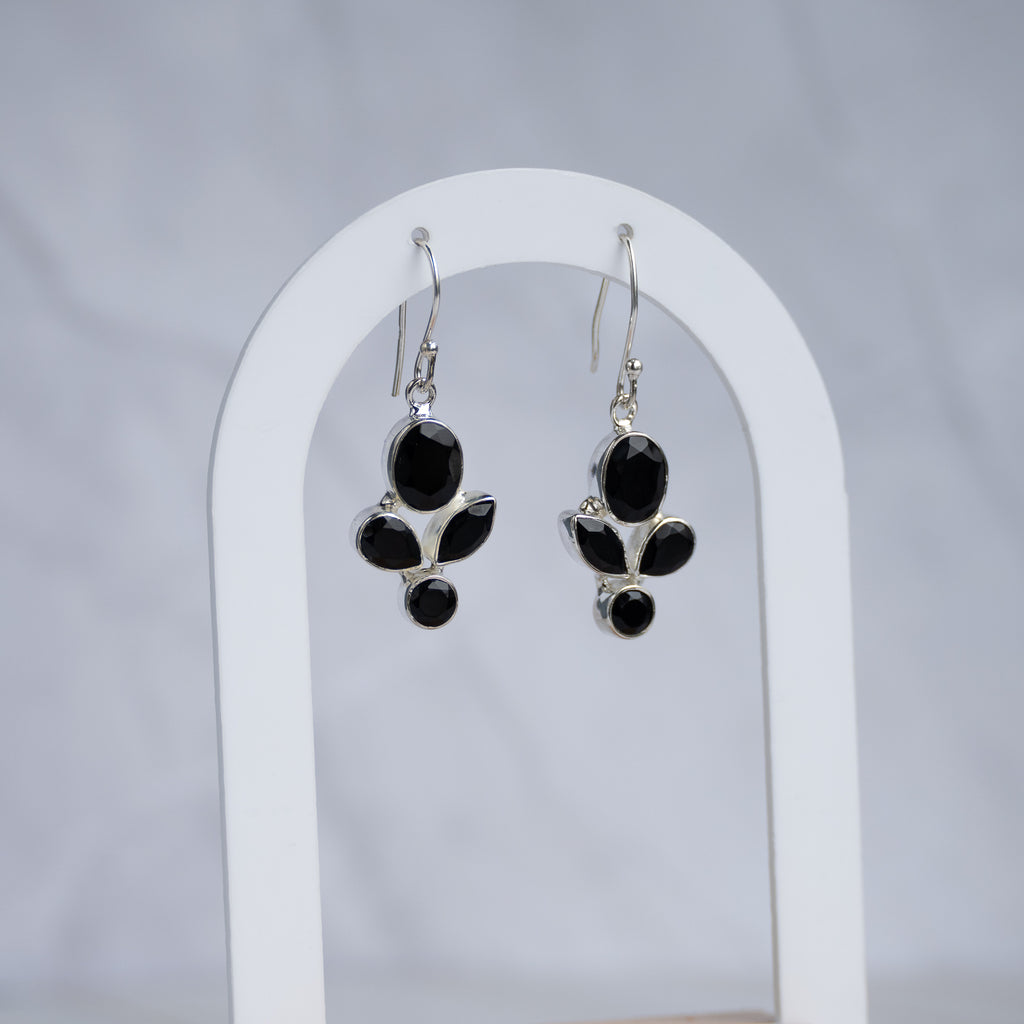 A pair of silver dangle earrings with black onyx stones, displayed on a white arched stand against a light gray background.