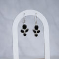 A pair of silver dangle earrings with black onyx stones, displayed on a white arched stand against a light gray background.