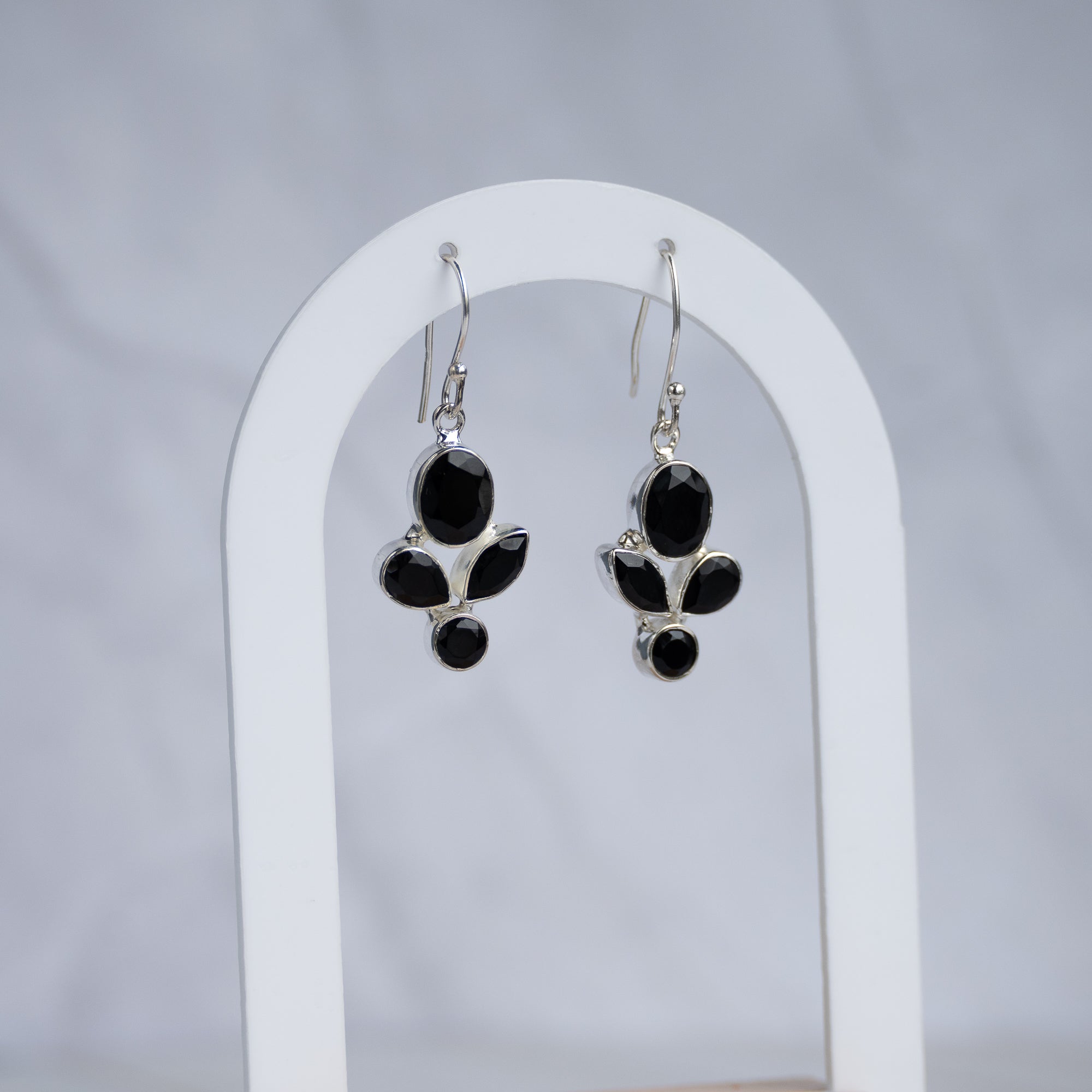 A pair of silver dangle earrings with black onyx stones, displayed on a white arched stand against a light gray background.