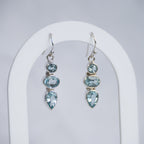 A pair of silver drop earrings with light blue gemstones, displayed on a white arched stand against a light gray background.