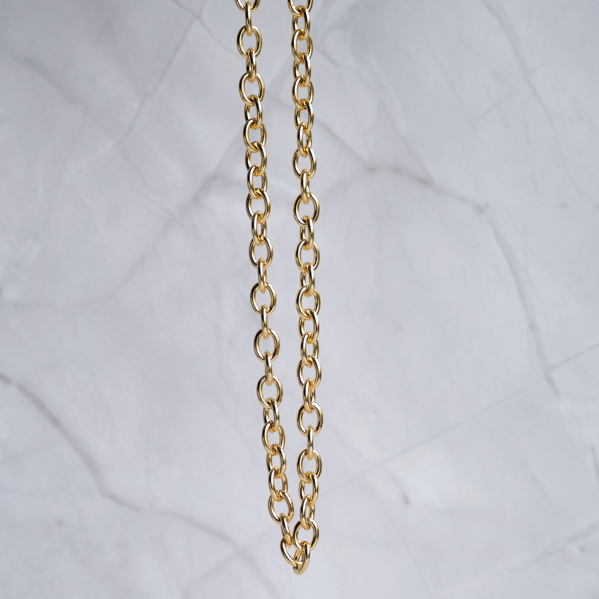 A close-up of a gold chain necklace hanging vertically against a light gray marble background.