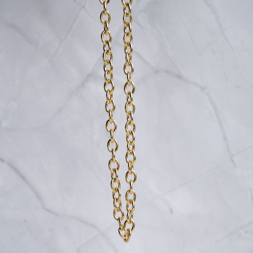 A close-up of a gold chain necklace hanging vertically against a light gray marble background.