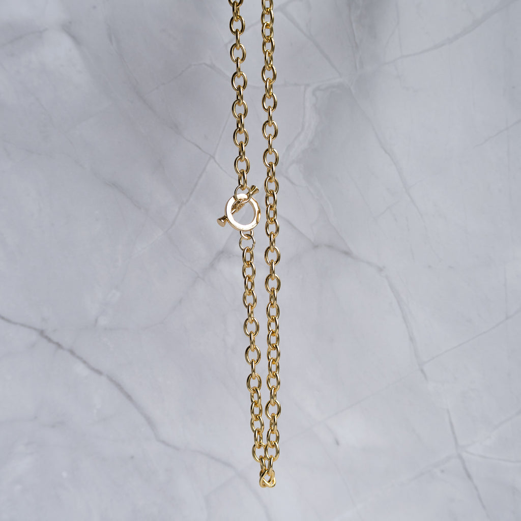 A close-up of a gold chain necklace with a lobster clasp, hanging against a light gray marble background.