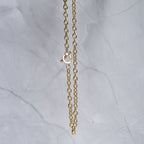 A close-up of a gold chain necklace with a lobster clasp, hanging against a light gray marble background.