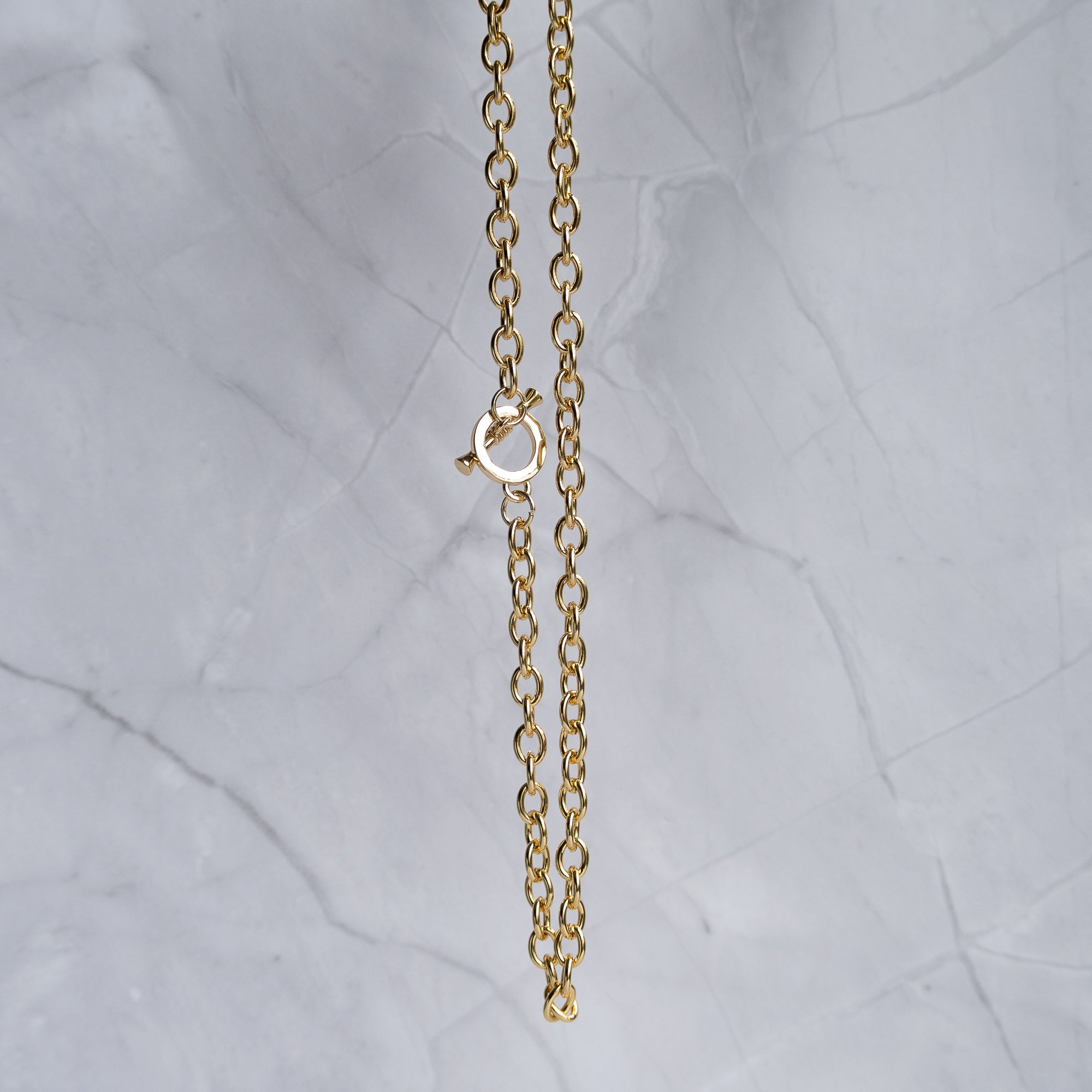 A close-up of a gold chain necklace with a lobster clasp, hanging against a light gray marble background.