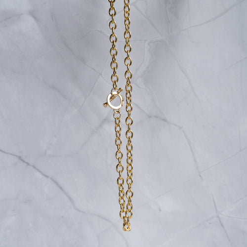 A close-up of a gold chain necklace with a lobster clasp, hanging against a light gray marble background.