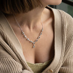 A close-up of a woman wearing a delicate silver necklace with clear teardrop-shaped crystals and a central teardrop pendant, styled with a beige cardigan.