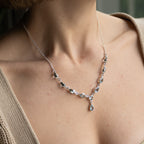 A close-up of a model wearing a delicate silver necklace with small clear faceted beads and a teardrop-shaped clear pendant.