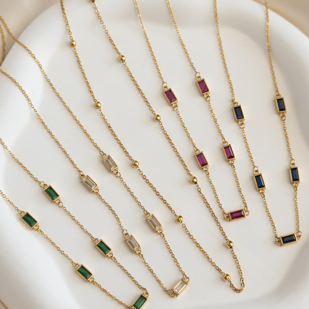 Gold necklaces with gemstone pendants on a white surface