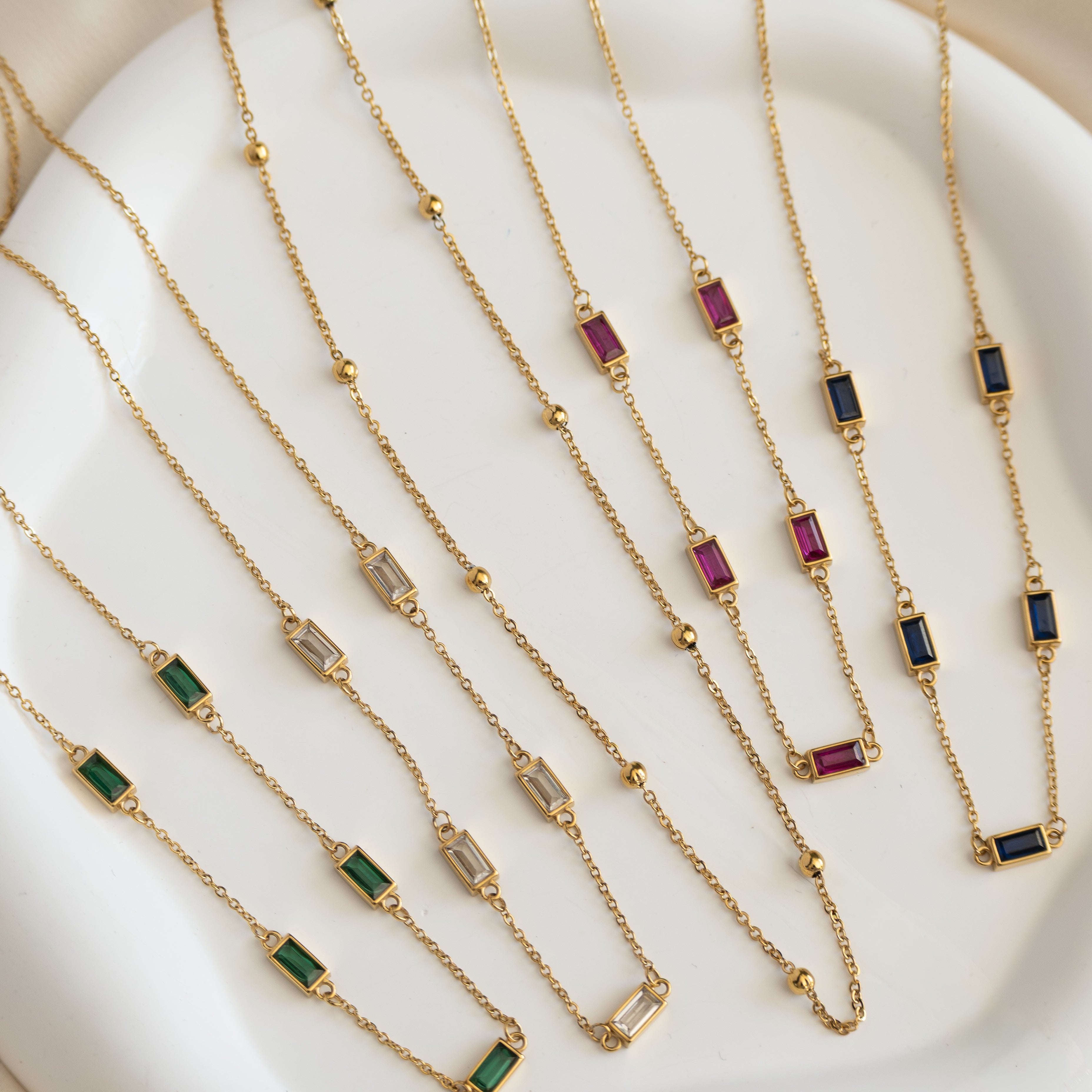 Gold necklaces with gemstone pendants on a white surface