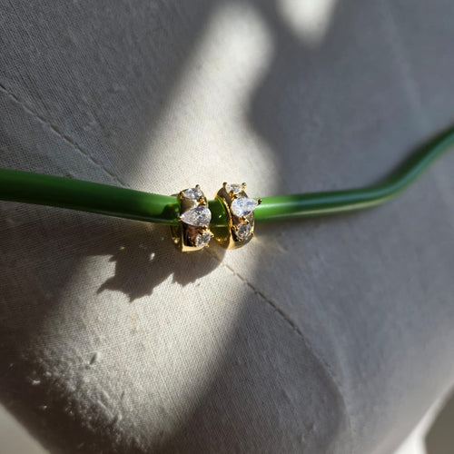 Gold earring with clear stones on a green stem against a light gray background