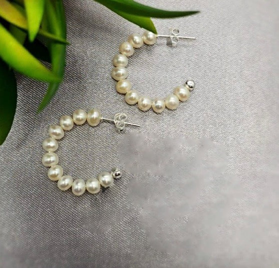 A pair of sterling silver hoop earrings adorned with freshwater pearls, displayed on a textured background.