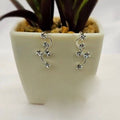 A pair of sterling silver creeper earrings with cubic zirconia drops placed on a white surface, partially in view of a potted plant.