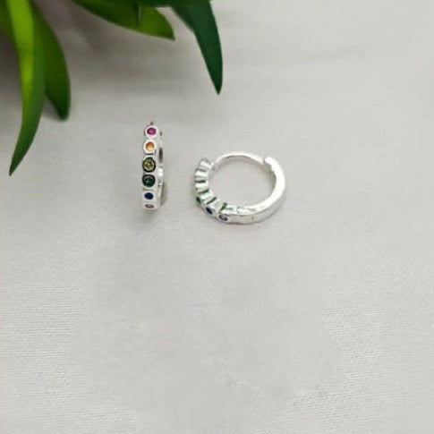 A pair of sterling silver huggie earrings with rainbow-colored cubic zirconia, displayed against a light background.