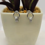 A pair of sterling silver double ring studs with cubic zirconia detail, displayed against a white pot with a plant.