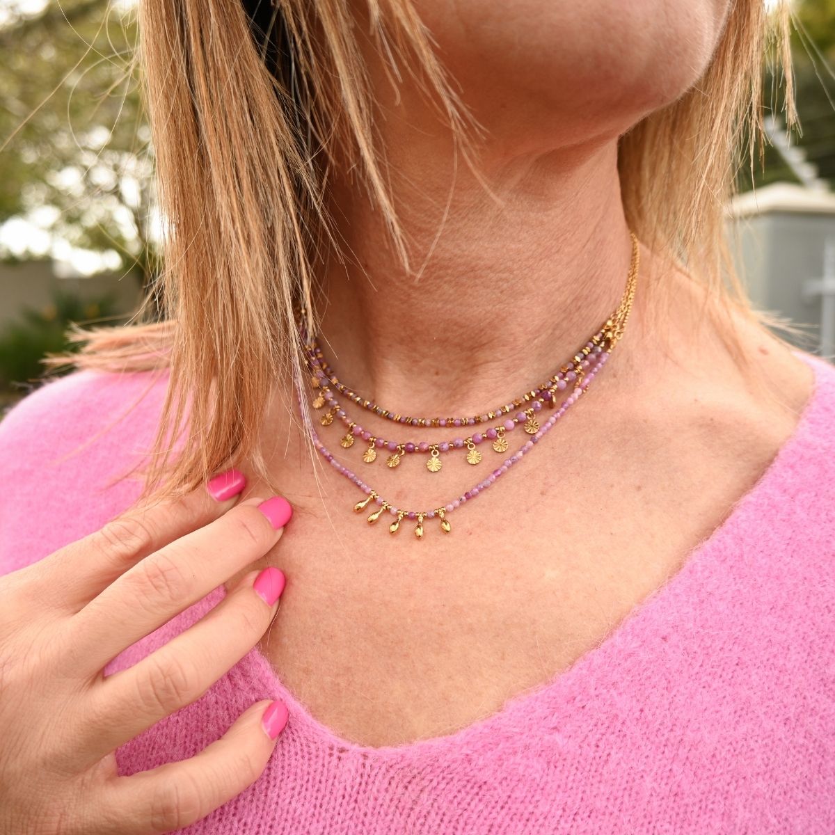 Close-up of a person wearing a necklace with a blurred outdoor background