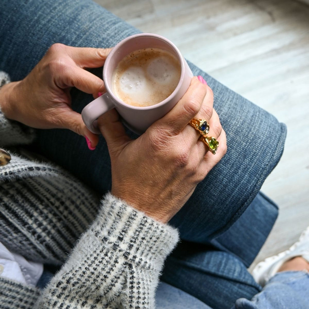 Person holding a pink mug with a drink, wearing a ring, sitting on a couch.