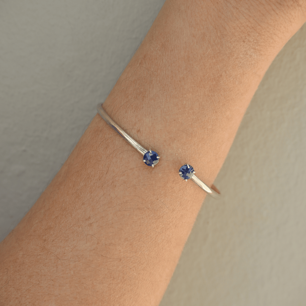 Silver bracelet with blue gemstones on a wrist against a neutral background