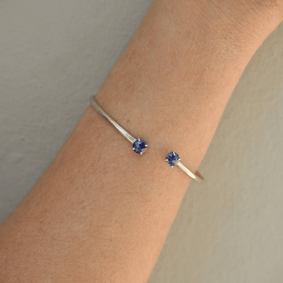 Silver bracelet with blue gemstones on a wrist against a neutral background