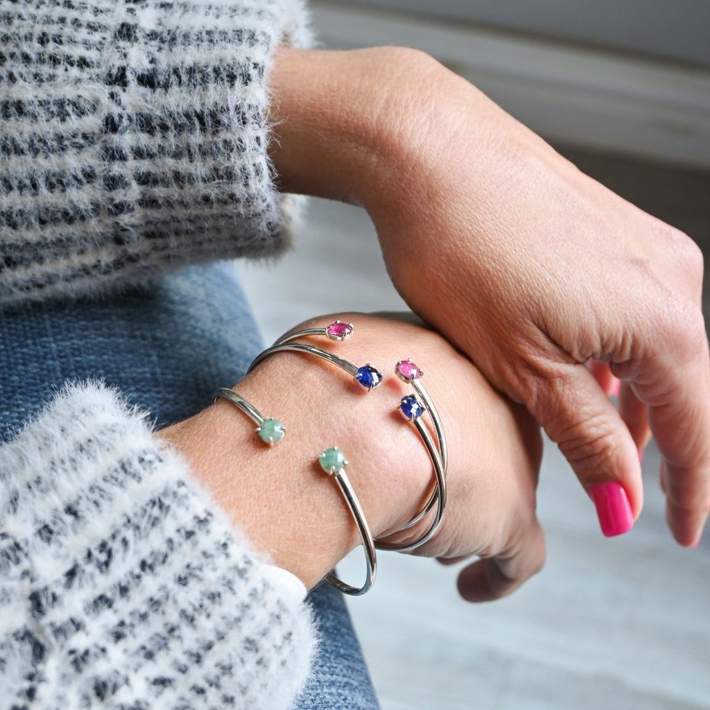 Close-up of a hand wearing multiple silver bracelets with colorful gemstones.