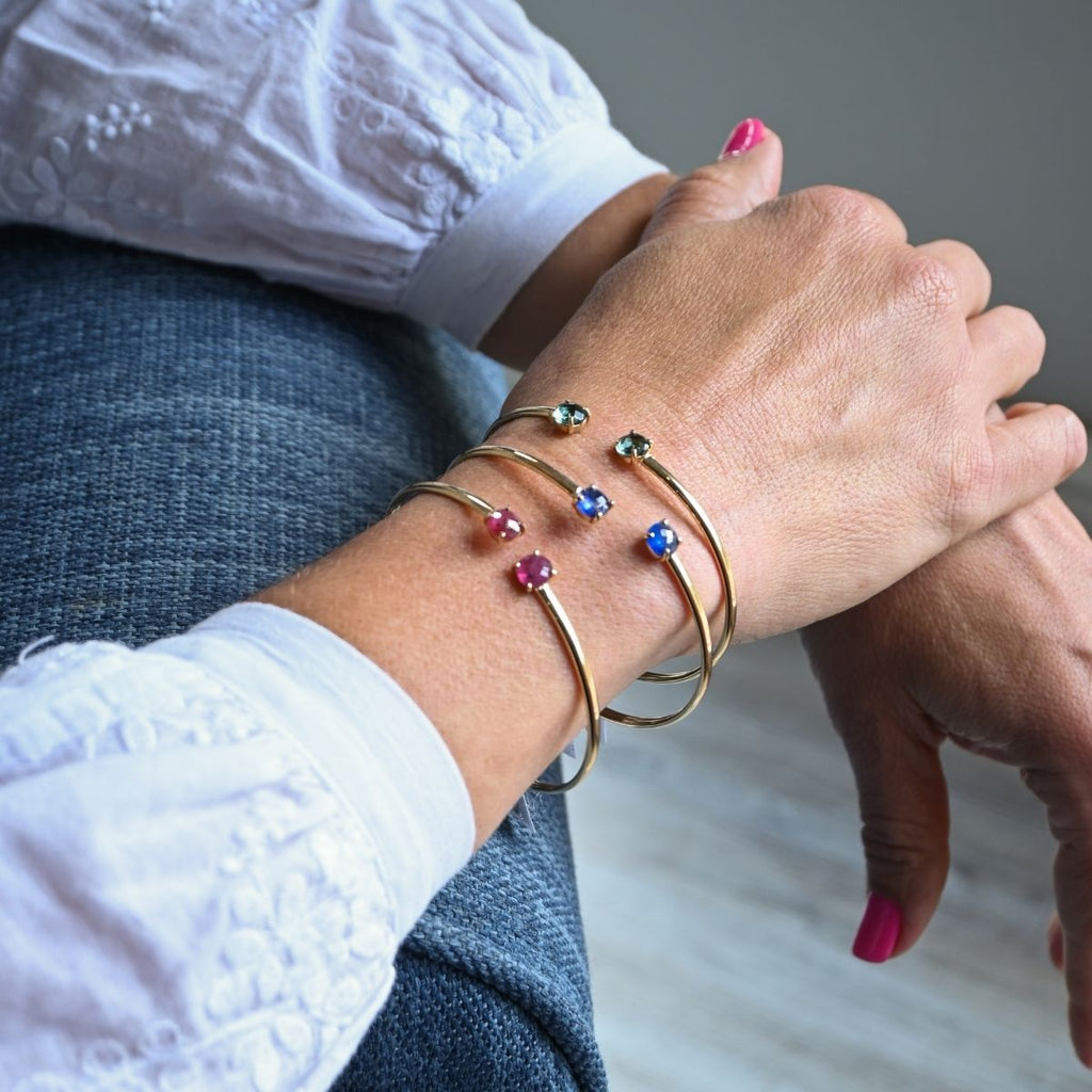 Close-up of a person's wrist wearing gold bracelets with colorful gemstones.