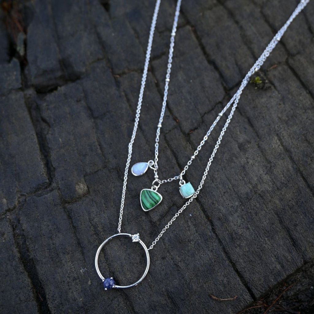 Silver necklace with heart and circle pendants on a dark stone surface
