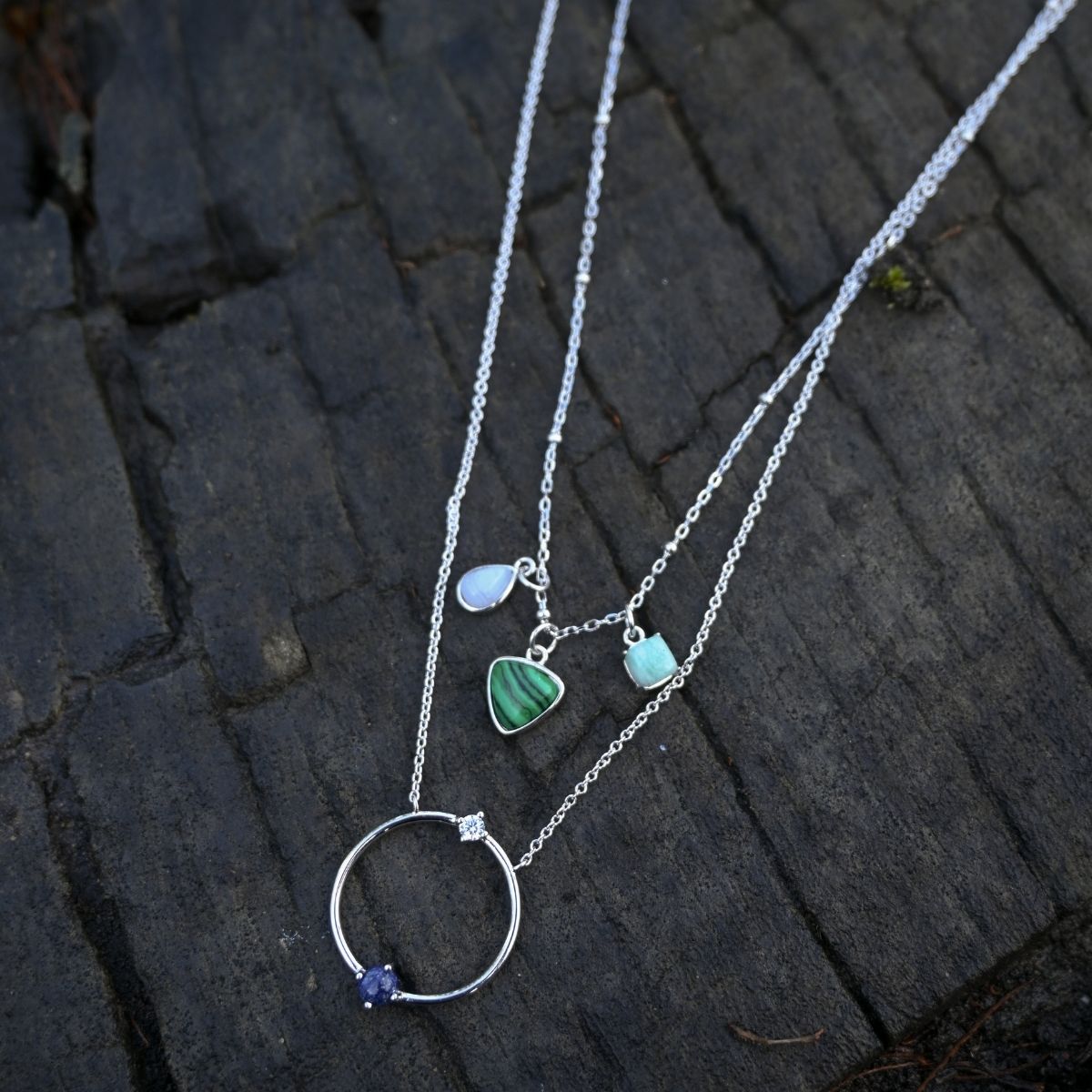 Silver necklace with heart and circle pendants on a dark stone surface