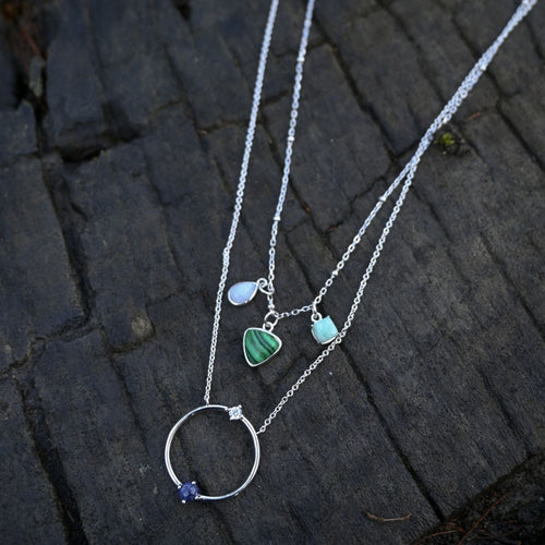 Silver necklace with heart and circle pendants on a dark stone surface