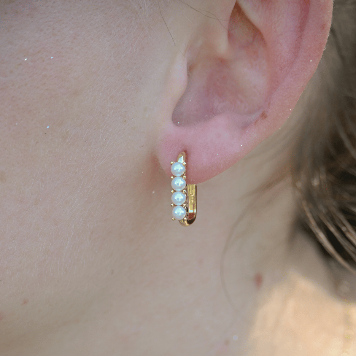 Gold hoop earring with pearls worn by a person