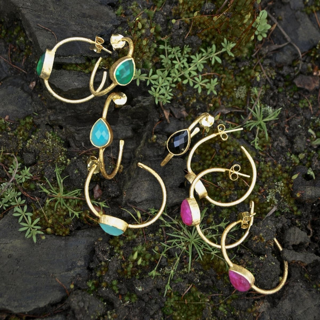 Gold earrings with colorful gemstones on a natural stone background