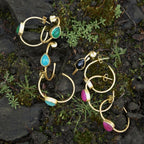 Gold earrings with colorful gemstones on a natural stone background