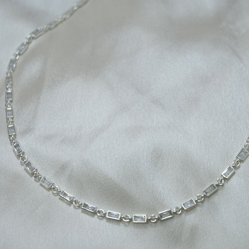 Silver necklace with rectangular gemstones on a white fabric background