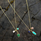 Gold necklace with colorful pendant charms on a stone surface