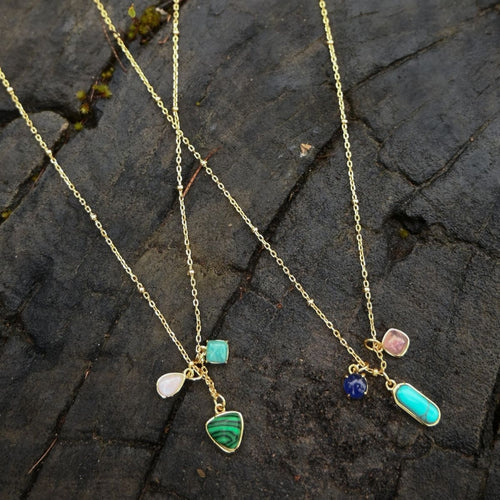 Gold necklace with colorful pendant charms on a stone surface