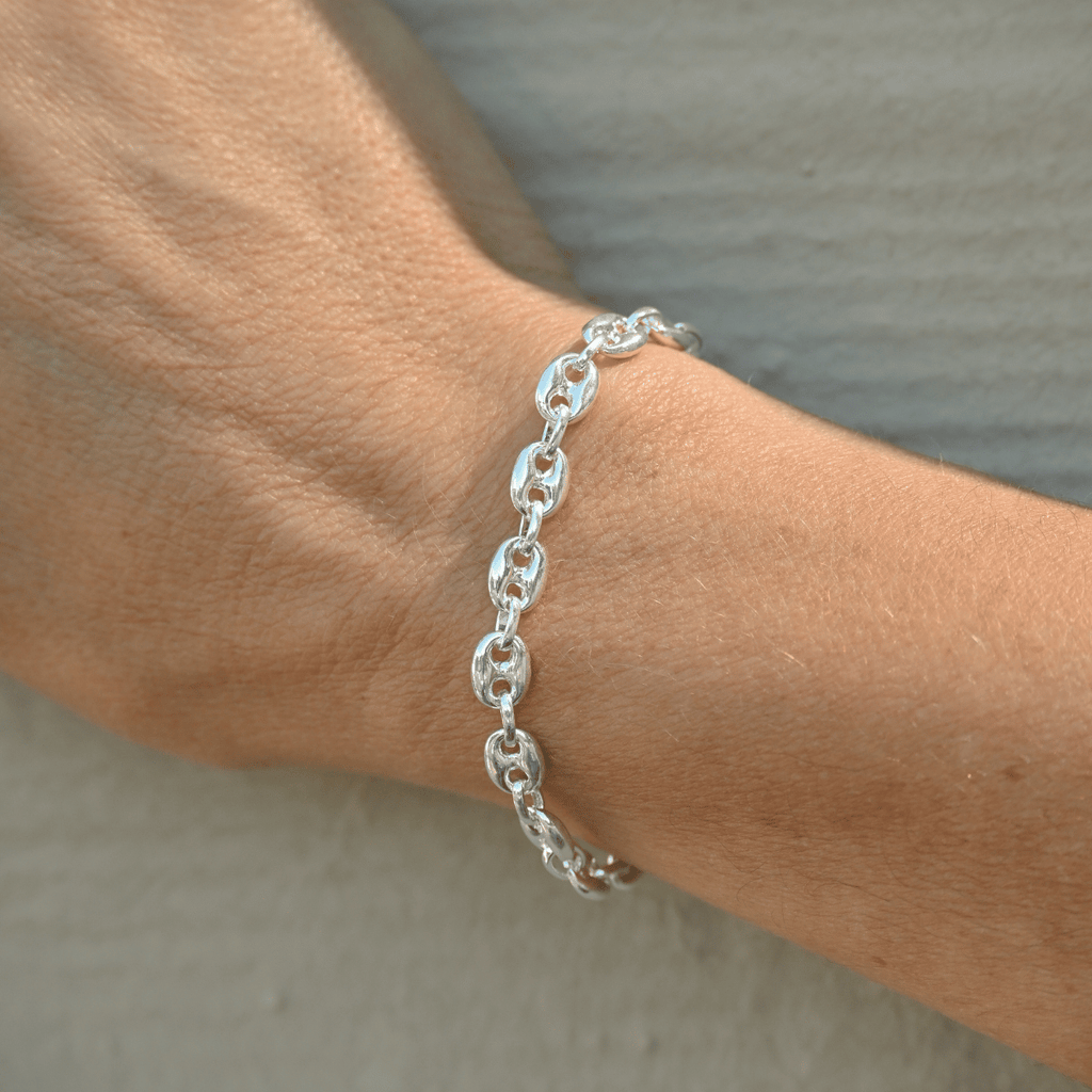 Silver chain bracelet on a wrist against a neutral background