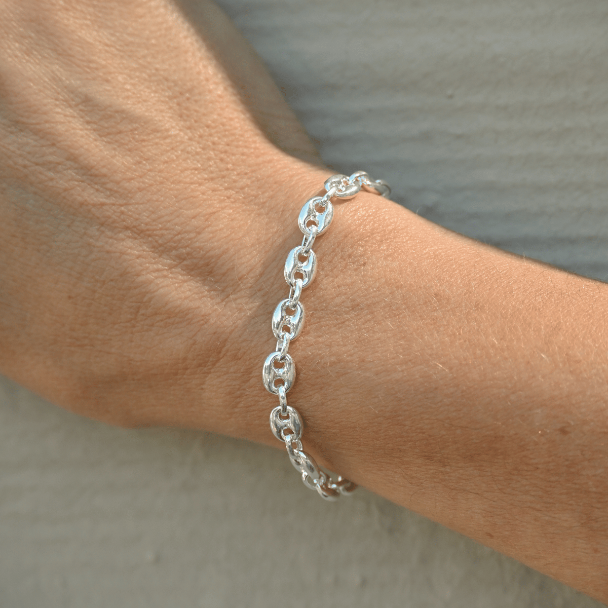 Silver chain bracelet on a wrist against a neutral background